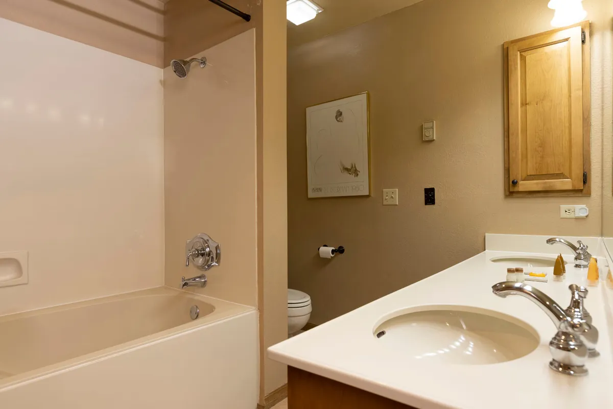 A calming bathroom scene with dual sinks, a spacious bathtub, and tasteful wall art. The setup is both practical and soothing, offering a perfect spot for self-care routines or a relaxing bath after a mountain adventure.