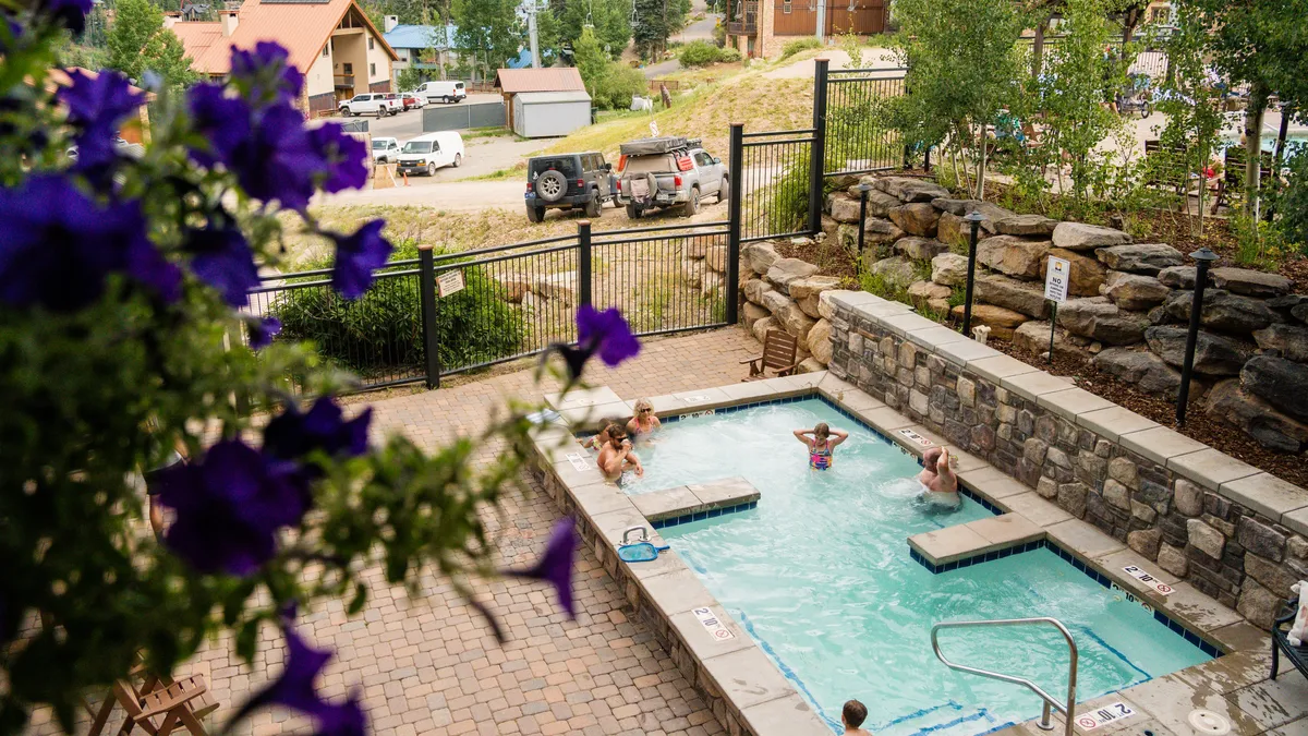 A lively outdoor swimming pool area with people relaxing and socializing. The pool is surrounded by blooming flowers, creating an inviting environment perfect for unwinding after a day of exploration.