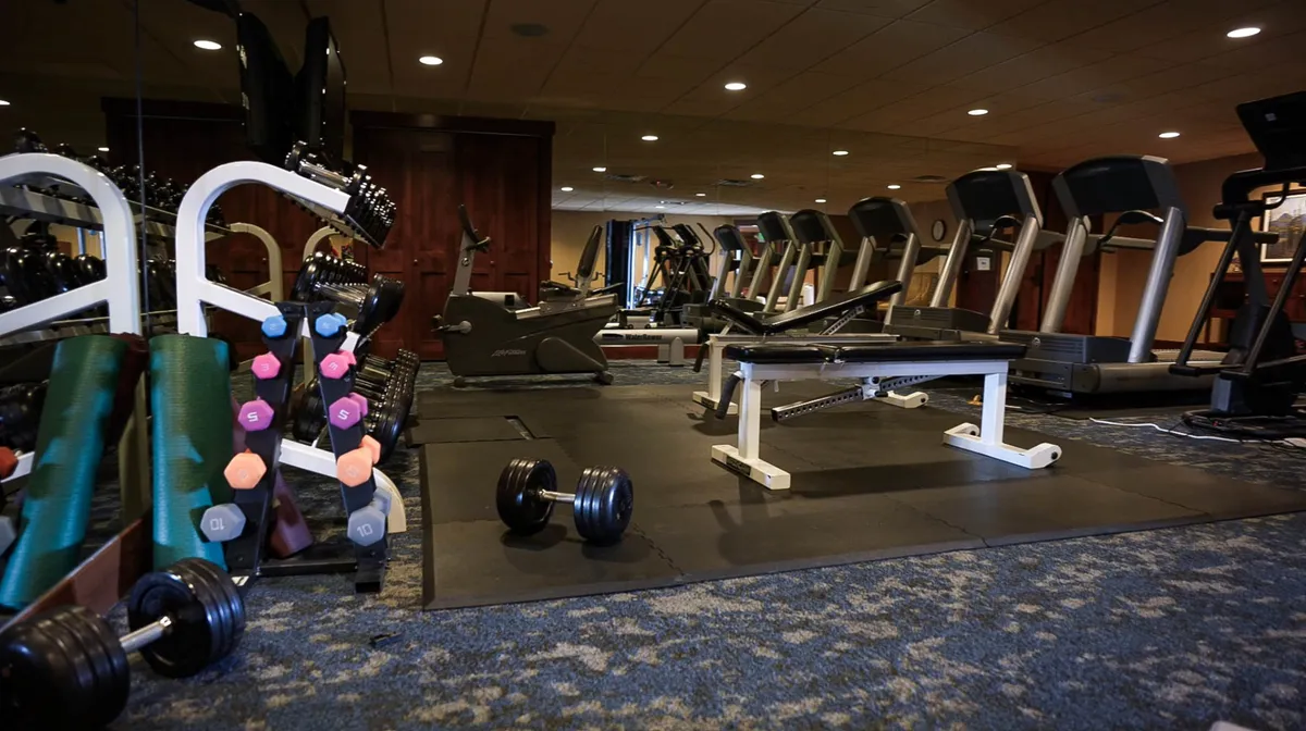 A modern fitness center with dumbbells, treadmills, and an exercise bench, set up for both solo and group workouts. The space is bright and motivational, highlighting an array of equipment for different fitness levels. The inviting atmosphere encourages guests to start their days with an energizing workout.