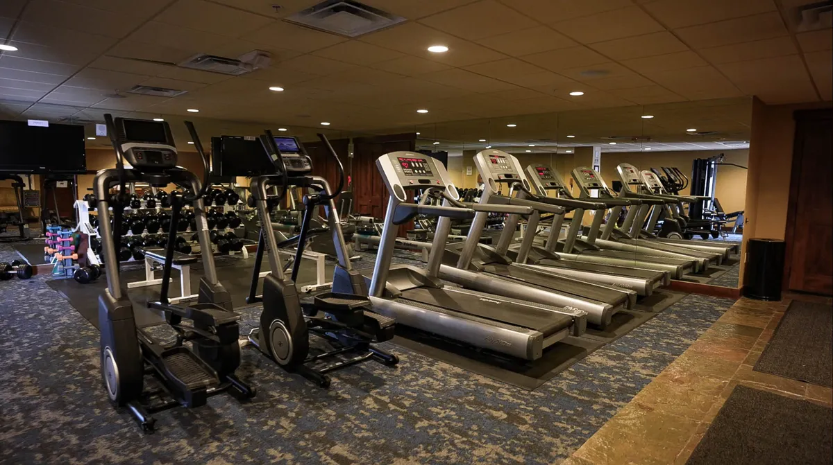 An interior image of a well-equipped fitness center with treadmills, ellipticals, dumbbells, and large mirrors. The space is energetic and designed for personal fitness, group classes, and wellness activities.
